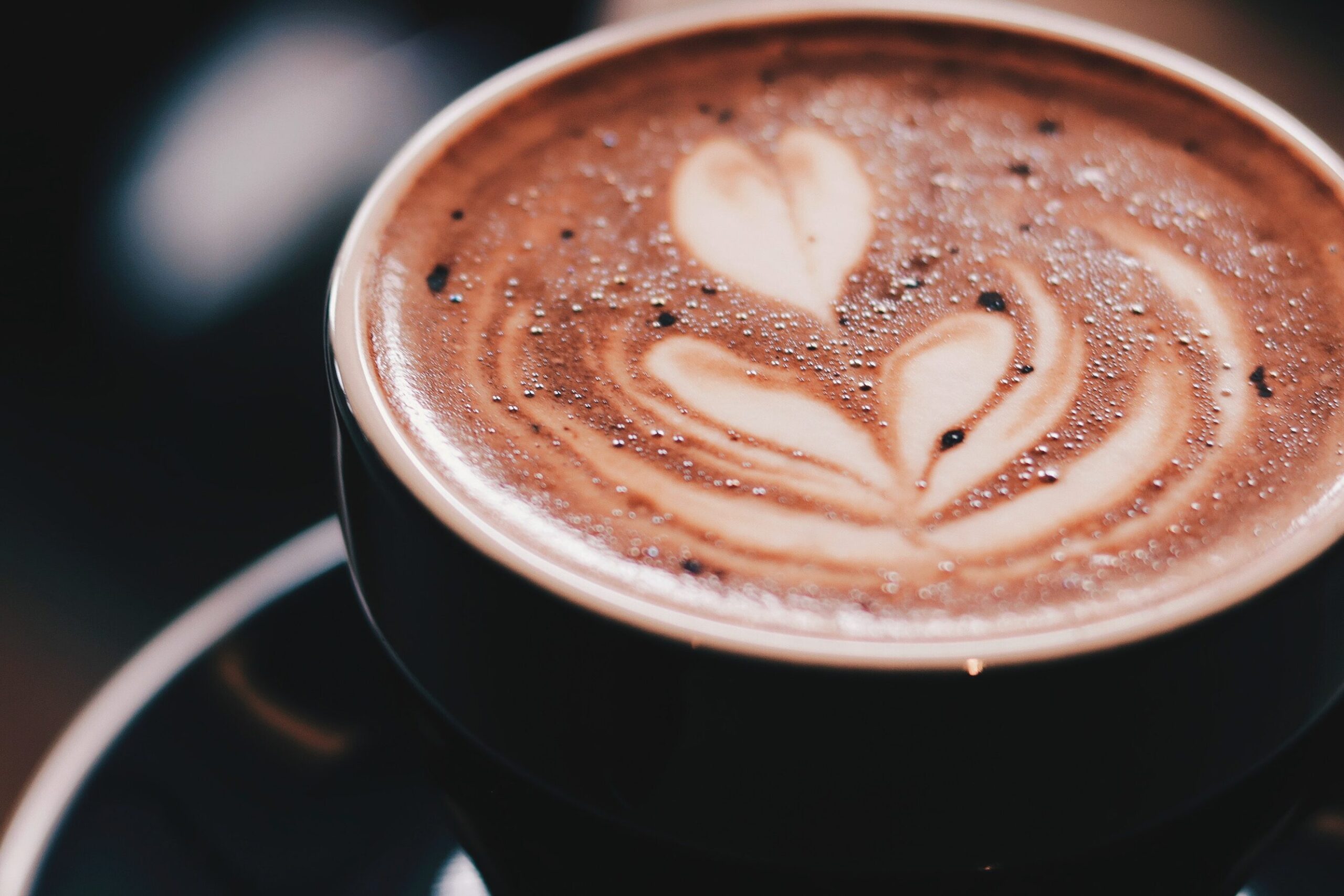 Fresh coffee dusted in chocolate in a black mug sitting on a saucer.